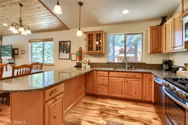 a kitchen with stainless steel appliances granite countertop a stove top oven a sink dishwasher and a refrigerator with wooden cabinets
