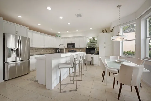 a kitchen with stainless steel appliances kitchen island granite countertop a refrigerator a stove a sink a dining table and chairs with wooden floor