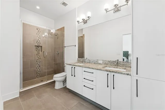 a bathroom with a granite countertop sink a toilet a mirror and shower