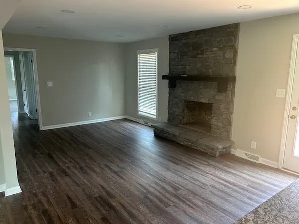 an empty room with wooden floor fireplace and windows
