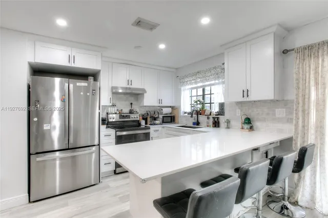 a kitchen with stainless steel appliances a refrigerator a sink a stove a dining table and chairs