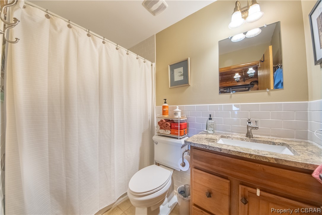 1239 Kelley Neck Road Lancaster, VA 22503 - Photo 37 of 48 Bathroom featuring toilet, vanity, tile walls, tile flooring, and backsplash
