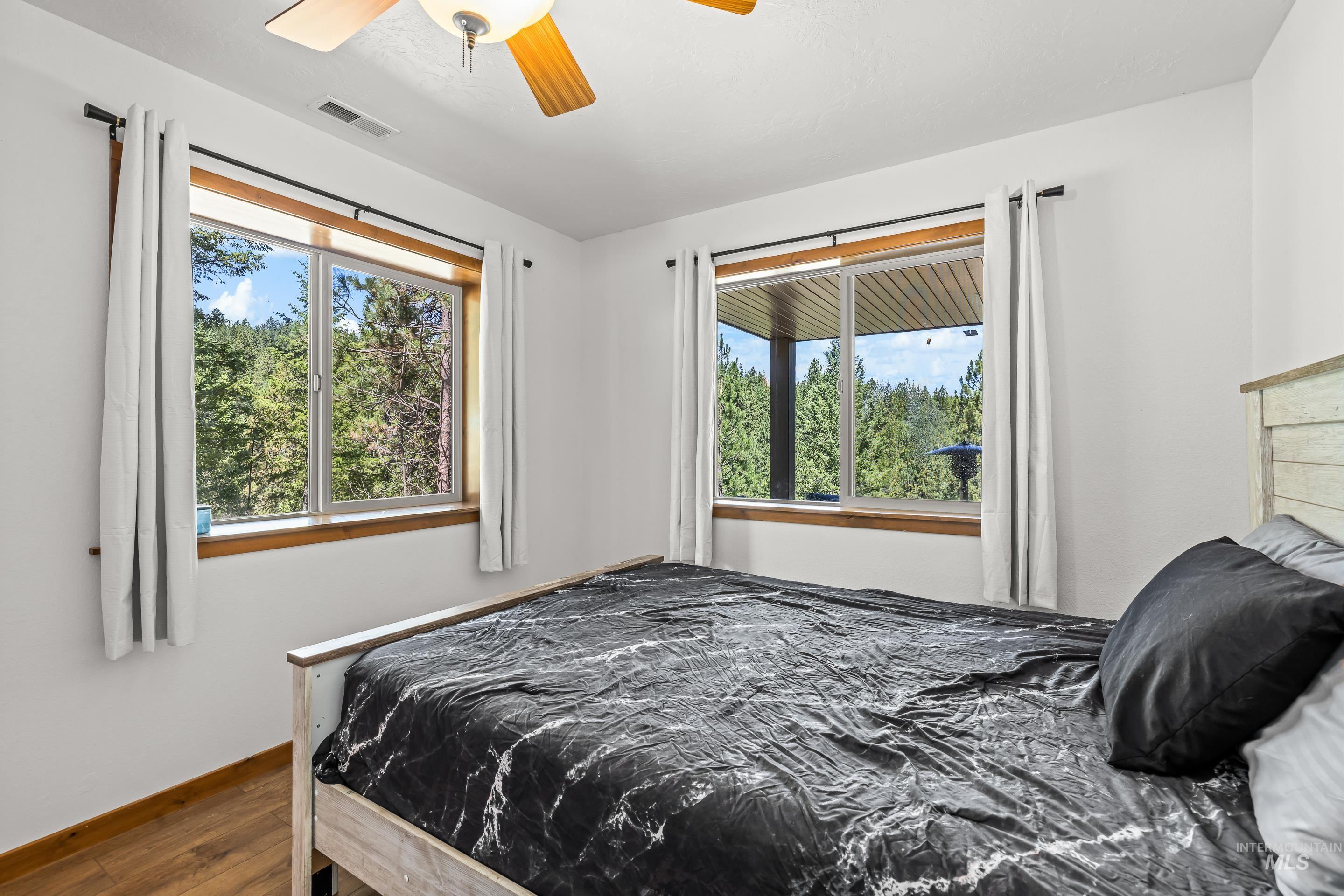 92 Cruickshank Road Horseshoe Bend, ID 83629 - Photo 27 of 50 Bright bedroom featuring wood-finish flooring, two large windows with natural wood trim, and a ceiling fan with light fixture