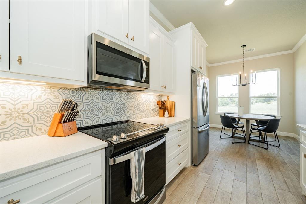 2000 Sweet Springs Road Weatherford, TX 76088 - Photo 11 of 40 a kitchen with stainless steel appliances a stove a sink and white cabinets with wooden floor