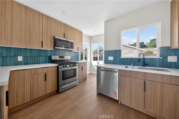 a kitchen with stainless steel appliances white cabinets a sink a stove a microwave and wooden floors
