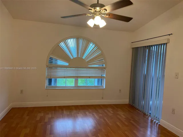 an empty room with wooden floor chandelier fan and windows