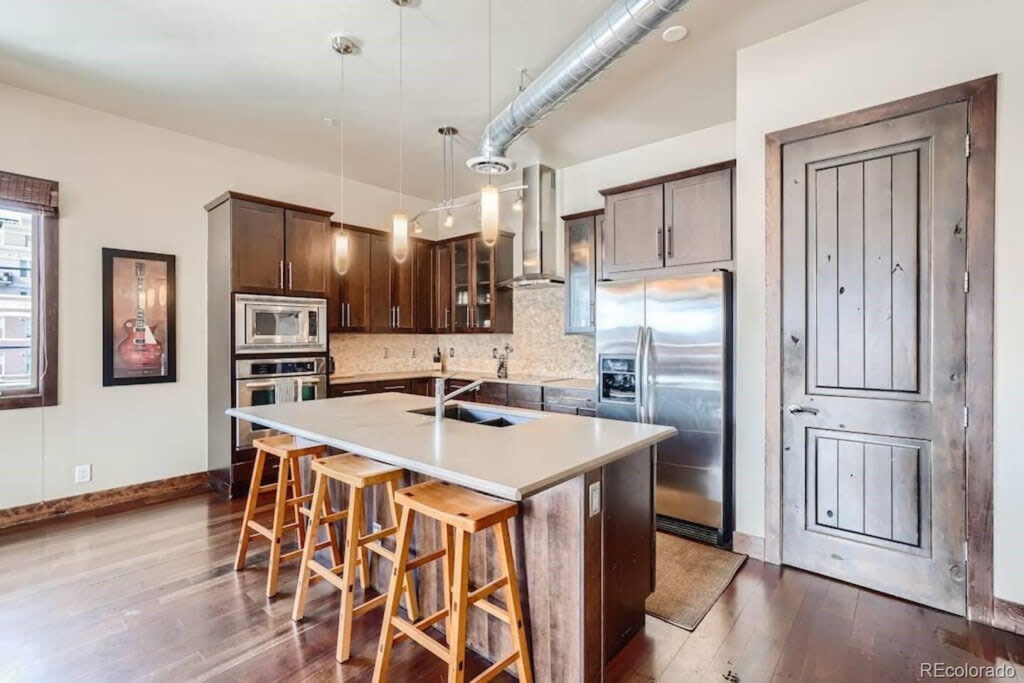 2101 Larimer Street, Unit 303 Denver, CO 80205 - Photo 3 of 21 a kitchen with stainless steel appliances granite countertop a refrigerator a stove a sink a dining table and chairs with wooden floor