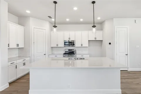 a large kitchen with stainless steel appliances a large counter top a stove a refrigerator and white cabinets with wooden floors