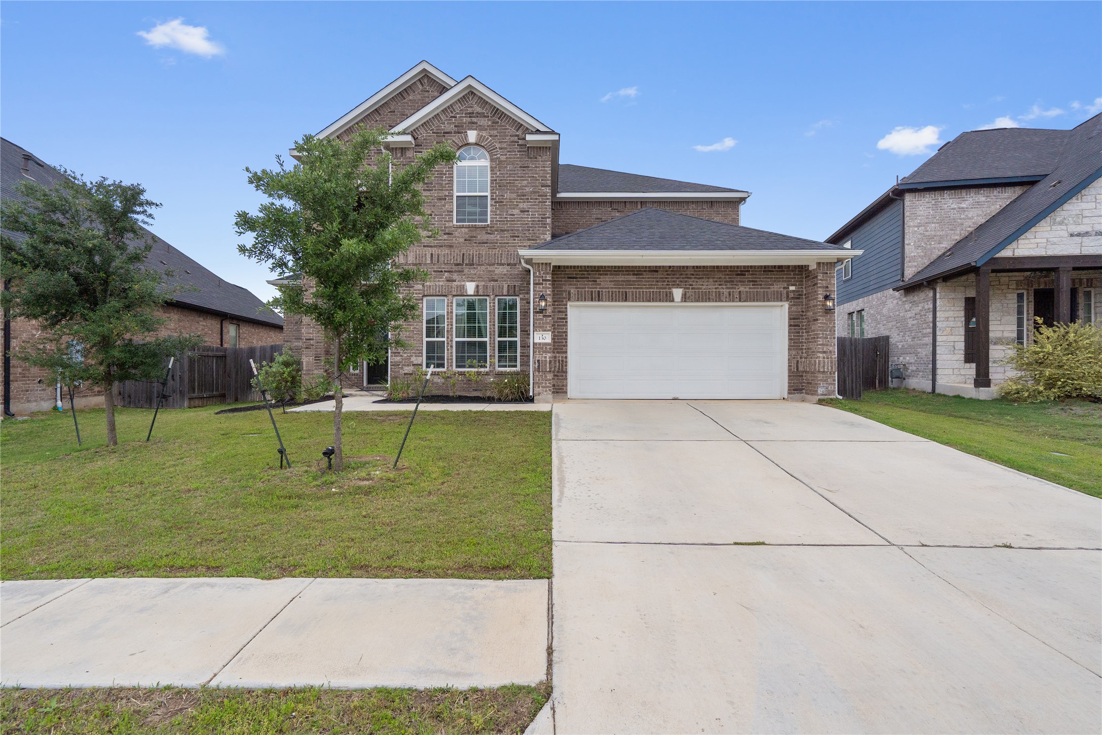 Brick facade residence featuring a two-car garage, concrete driveway, and front lawn with young trees