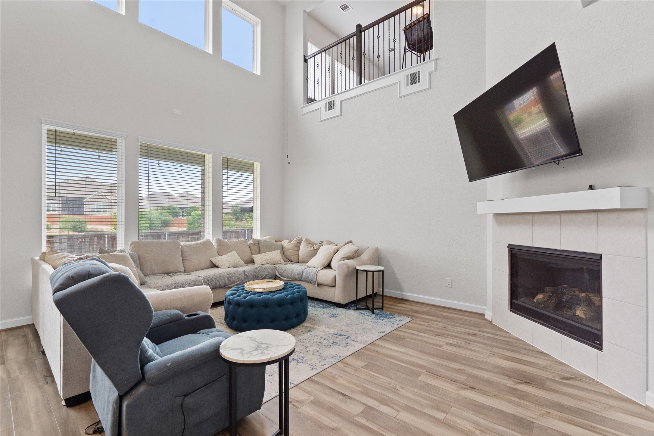 130 Wild Pecan Loop Buda, TX 78610 - Photo 11 of 31 Two-story living area featuring wood-finish flooring, a white tiled fireplace with a mantel, and multiple windows providing natural illumination