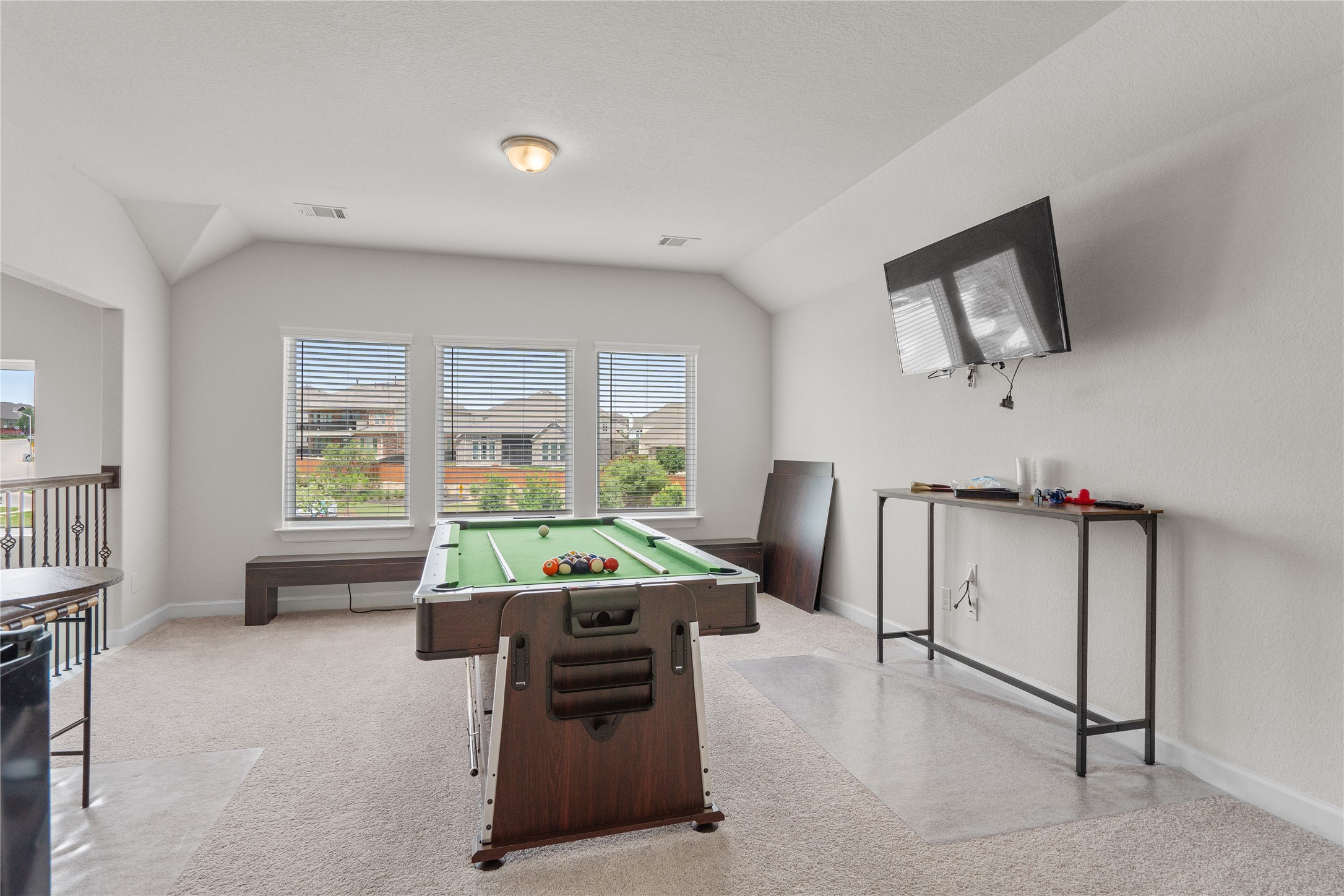 130 Wild Pecan Loop Buda, TX 78610 - Photo 24 of 31 Versatile bonus room featuring light-colored carpeting, multiple windows with blinds, a wall-mounted display, and an open railing overlooking a lower level