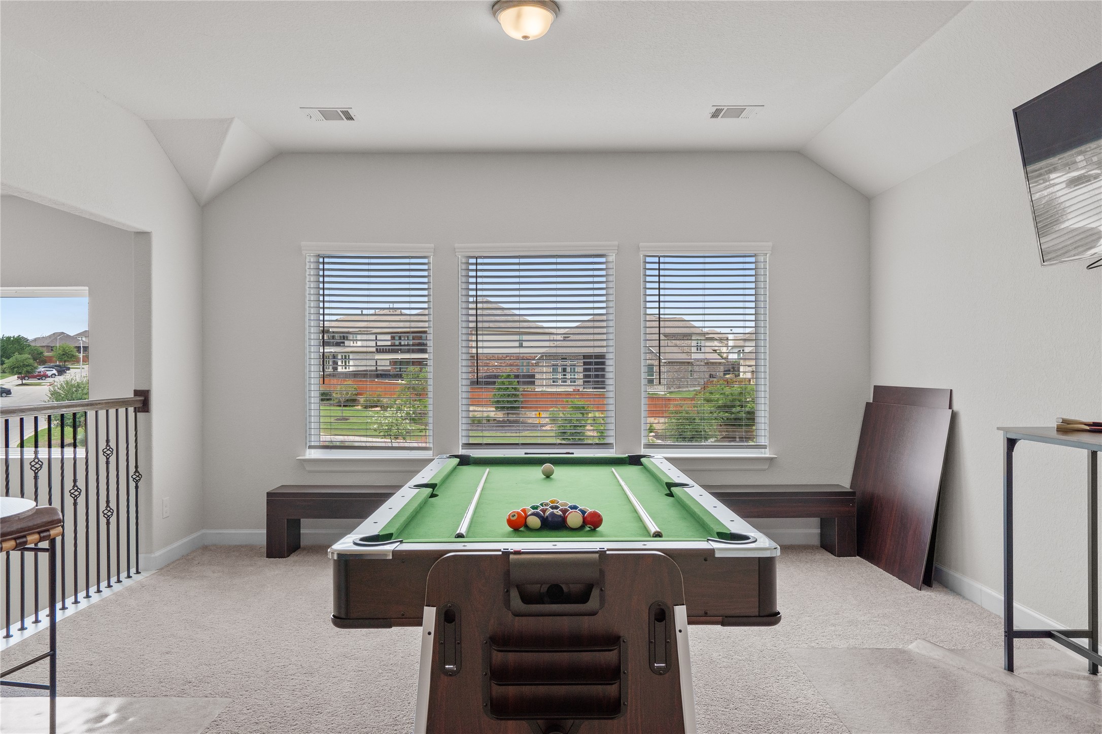 130 Wild Pecan Loop Buda, TX 78610 - Photo 25 of 31 Carpeted upstairs area featuring three windows with blinds, a vaulted ceiling, and an open railing with decorative metal spindles