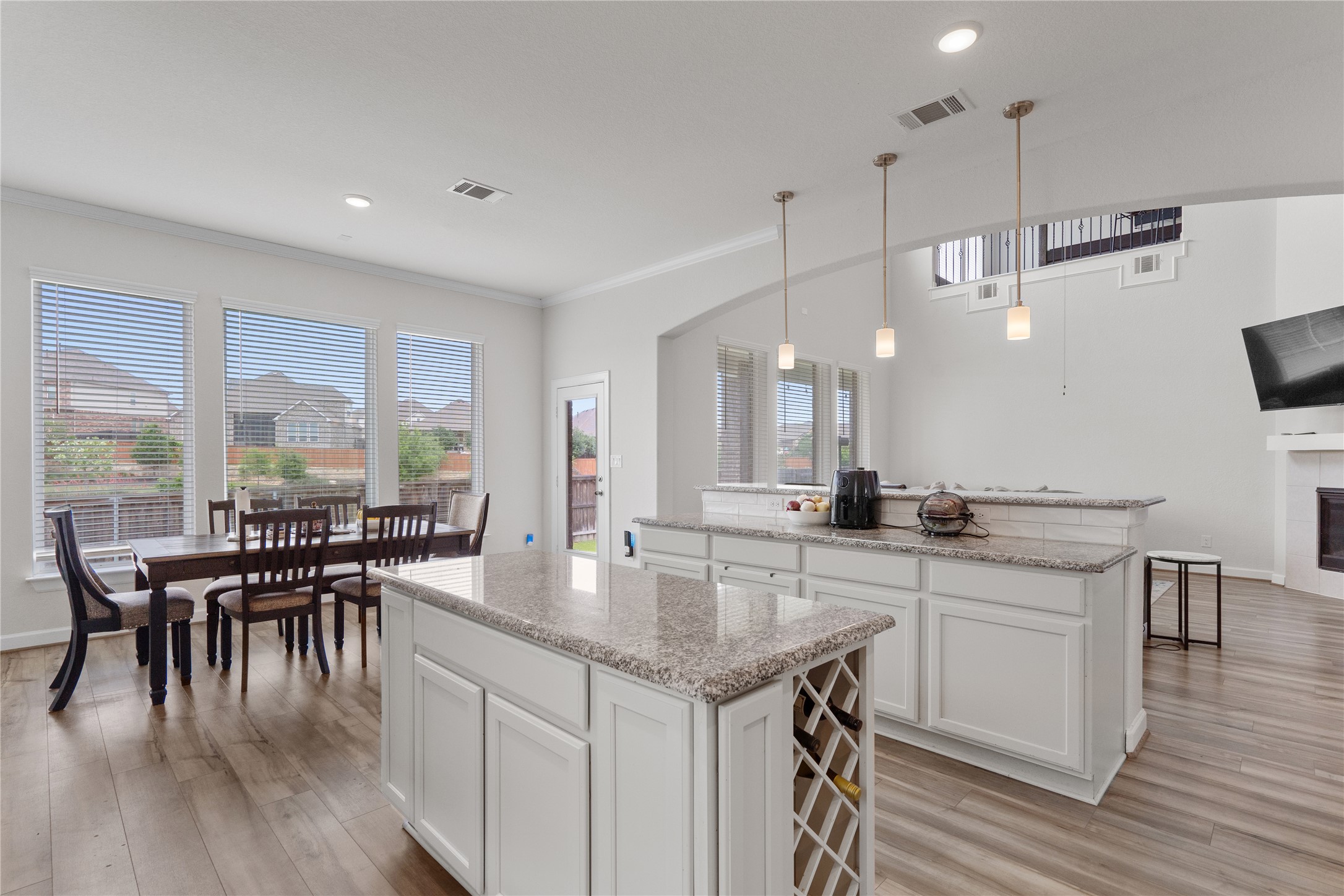 130 Wild Pecan Loop Buda, TX 78610 - Photo 6 of 31 Open-concept living area featuring wood-finish flooring, white cabinetry with granite countertops, a kitchen island with built-in wine storage, and pendant lighting