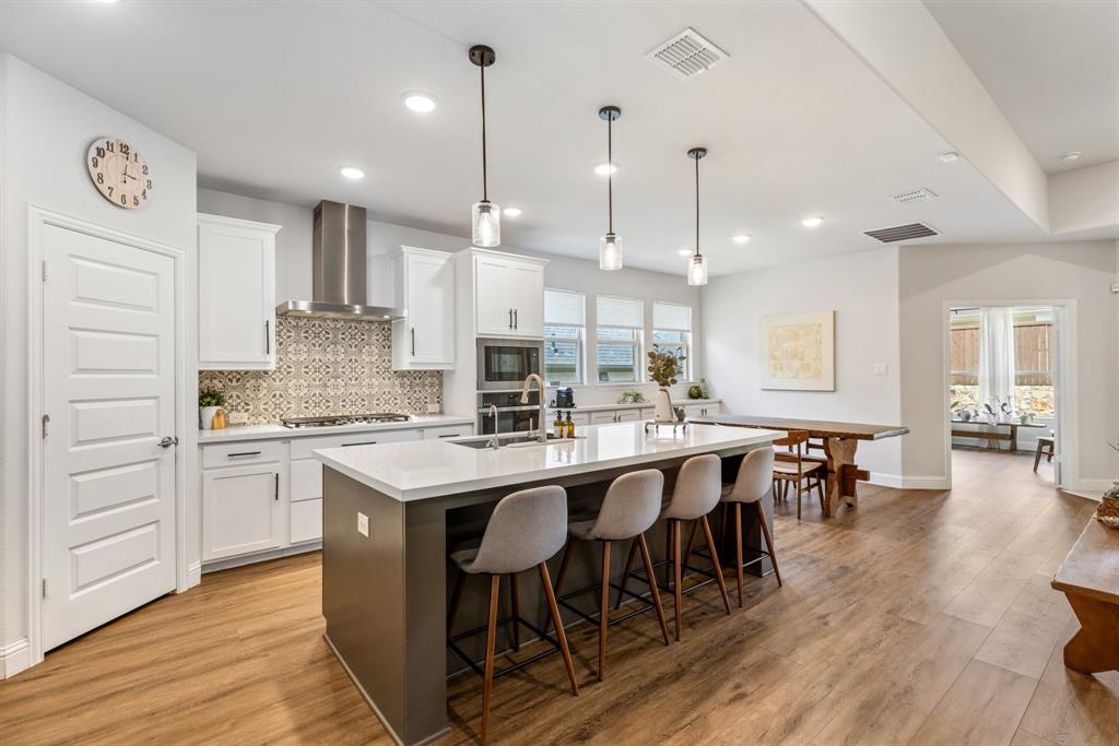 313 Savannah Lane Oak Point, TX 75068 - Photo 7 of 39 Kitchen with white cabinetry, decorative light fixtures, a center island with sink, a breakfast bar area, and light wood-style flooring