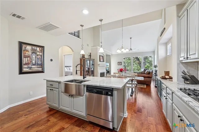 a kitchen with stainless steel appliances a stove a sink dishwasher and a dining table with wooden floor