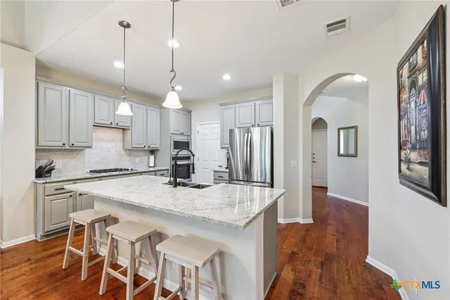 a kitchen with stainless steel appliances granite countertop a kitchen island a stove a refrigerator a sink a dining table and chairs with wooden floor