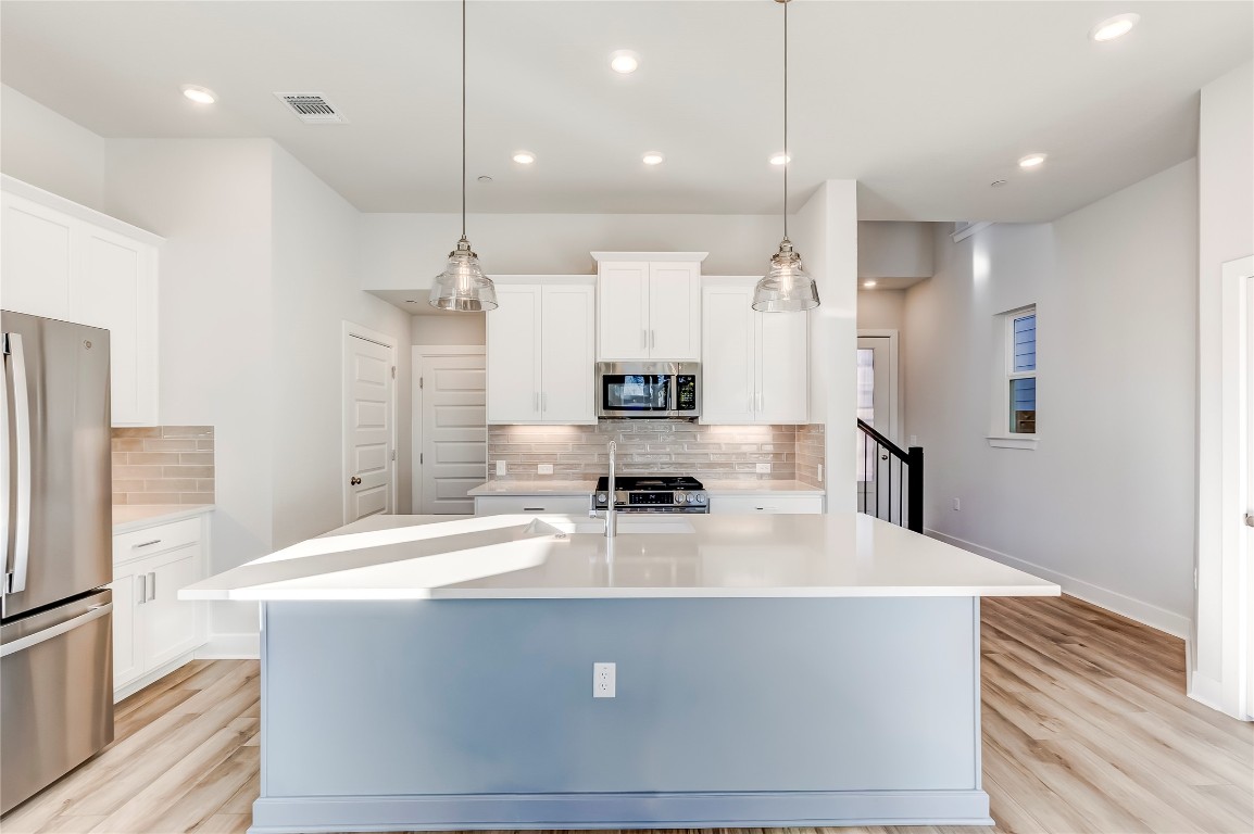 715 Bernese Pass Austin, TX 78745 - Photo 11 of 38 Kitchen with stainless steel appliances, a center island with sink, white cabinets, decorative light fixtures, and recessed lighting