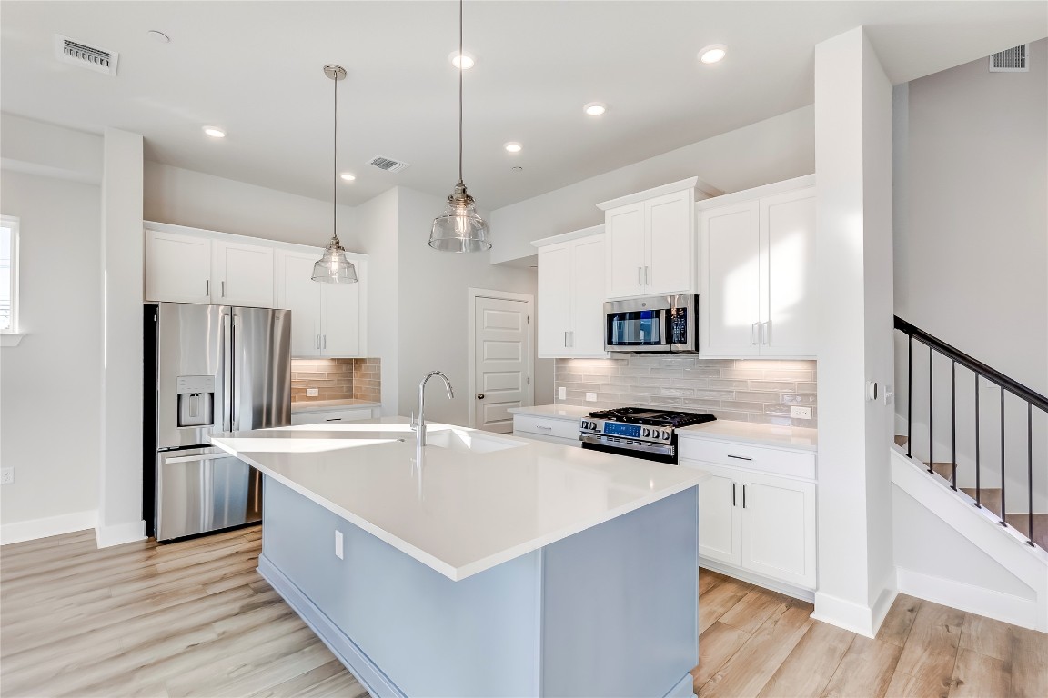715 Bernese Pass Austin, TX 78745 - Photo 12 of 38 Kitchen featuring stainless steel appliances, a kitchen island with sink, white cabinetry, pendant lighting, and backsplash