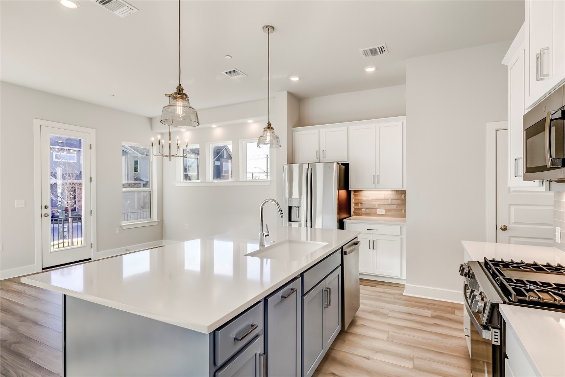 715 Bernese Pass Austin, TX 78745 - Photo 13 of 38 Kitchen with backsplash, white cabinetry, pendant lighting, light wood-style floors, and a center island with sink
