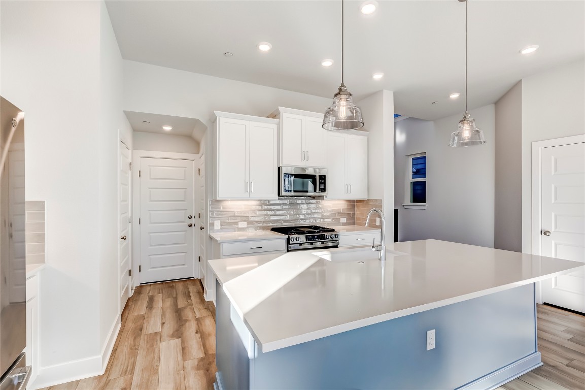 715 Bernese Pass Austin, TX 78745 - Photo 14 of 38 Kitchen featuring a kitchen island with sink, hanging light fixtures, white cabinets, stainless steel appliances, and tasteful backsplash