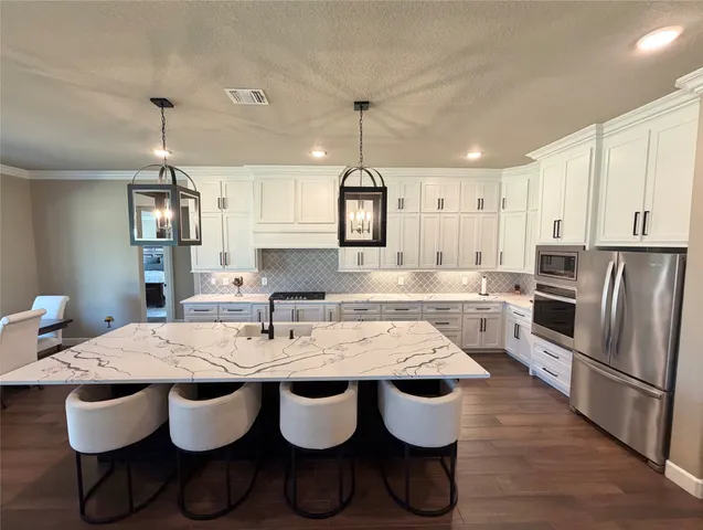 a kitchen with granite countertop lots of wooden cabinets stainless steel appliances and chandelier