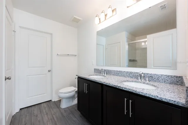 a bathroom with a granite countertop sink a toilet a large mirror and shower