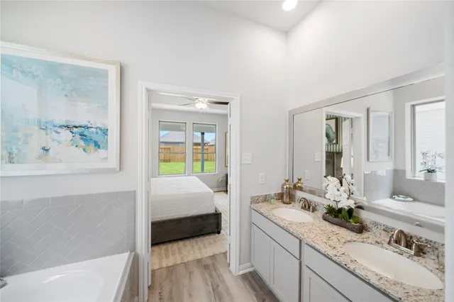 a en suite bathroom with a granite countertop tub a double vanity sink and a window