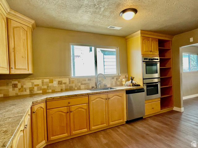 255 West Main Street Mount Pleasant, UT 84647 - Photo 5 of 35 Kitchen featuring light wood-finish cabinetry, a stainless steel double wall oven, a stainless steel dishwasher, wood-finish flooring, and a tiled backsplash