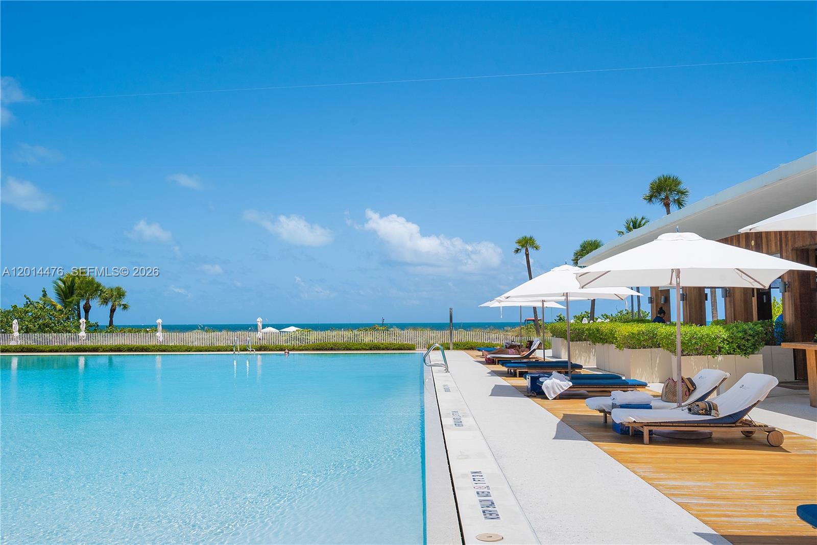 360 Ocean Drive, Unit 1106S Key Biscayne, FL 33149 - Photo 35 of 67 Pool Deck – A sunlit pool deck includes chaise lounges, umbrellas, and wood deck accents overlooking the water. The layout offers an inviting outdoor space for relaxing beside the beach.