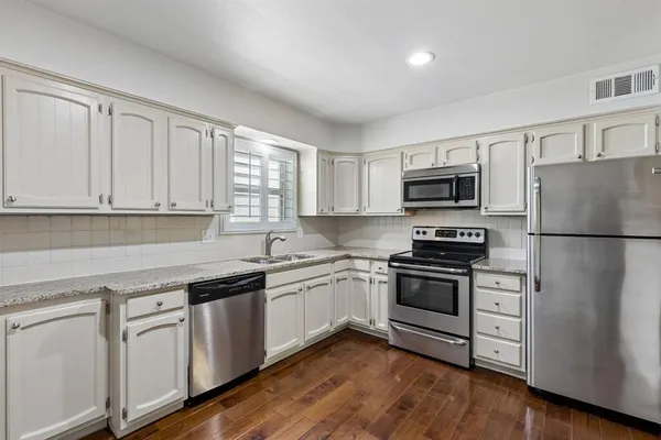 a kitchen with white cabinets appliances and wooden floor