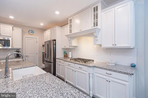 a large white kitchen with a large island oven a sink dishwasher and a couch with wooden floor