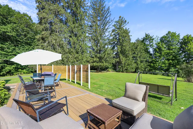 a view of a patio with couches table and chairs under an umbrella with large trees and big yard