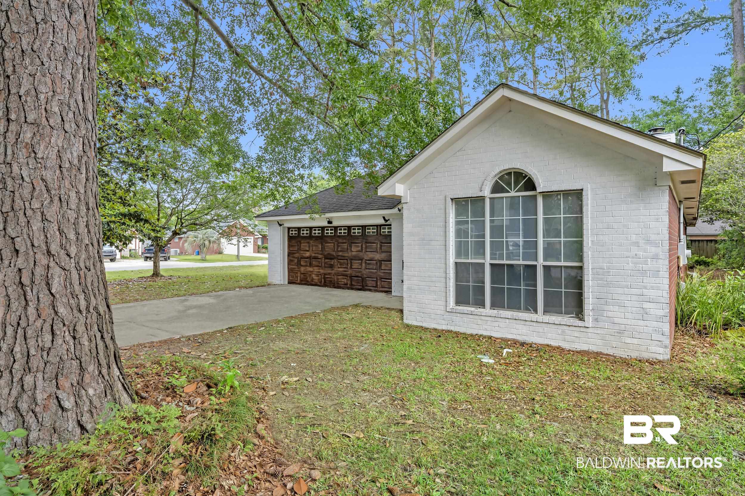 509 Loblolly Court Foley, AL 36535 - Photo 25 of 26 White brick exterior with a prominent arched window, a two-car garage featuring a wood-finish door, and mature trees providing natural shade