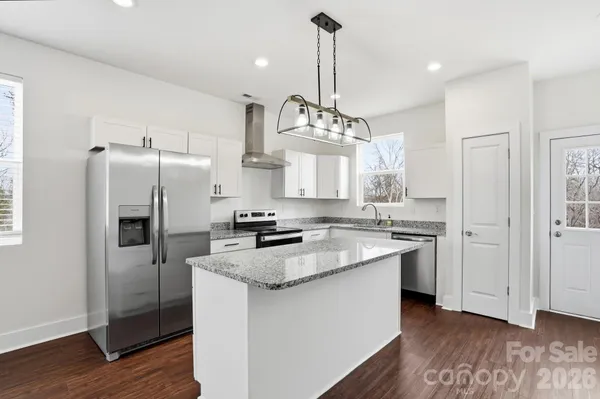 a kitchen with granite countertop a refrigerator a sink dishwasher a stove and a wooden floors