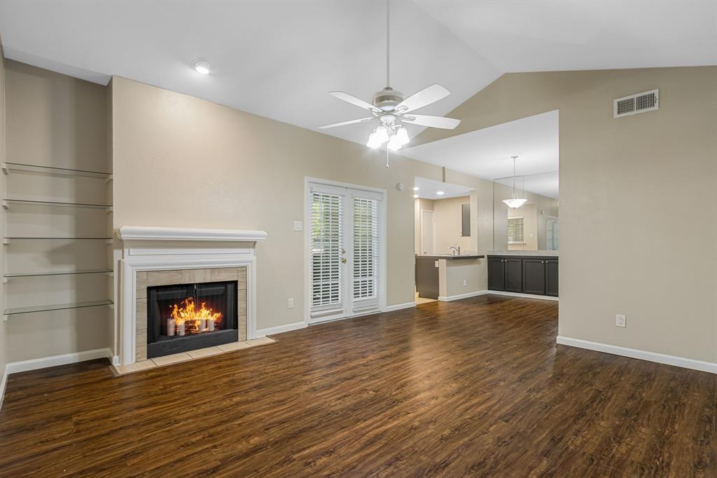 8601 Park Lane, Unit 221 Dallas, TX 75231 - Photo 3 of 26 Unfurnished living room with dark wood-style floors, vaulted ceiling, a tile fireplace, and a ceiling fan