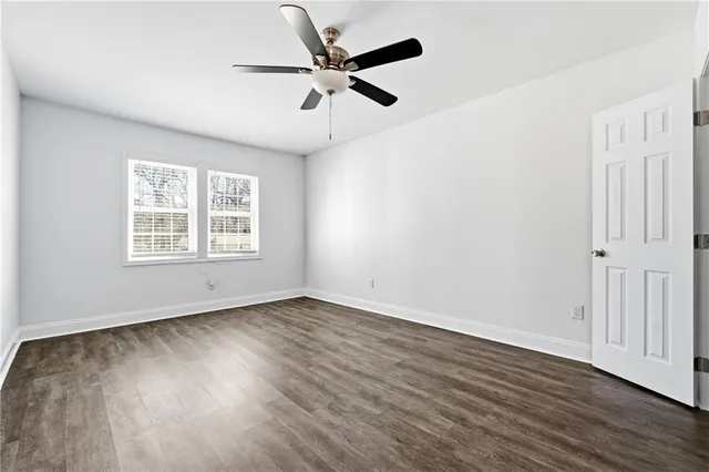 an empty room with wooden floor fan and windows