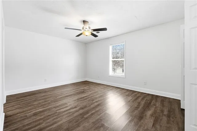 an empty room with wooden floor fan and windows