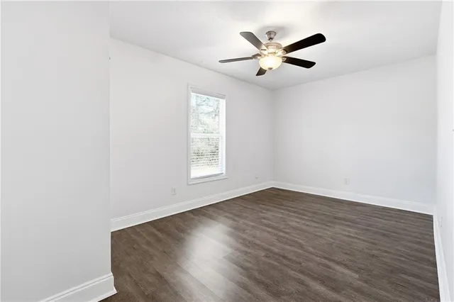 an empty room with wooden floor fan and windows