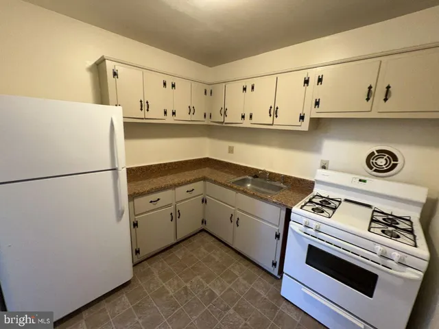 a white kitchen with stainless steel appliances granite countertop a stove and a refrigerator