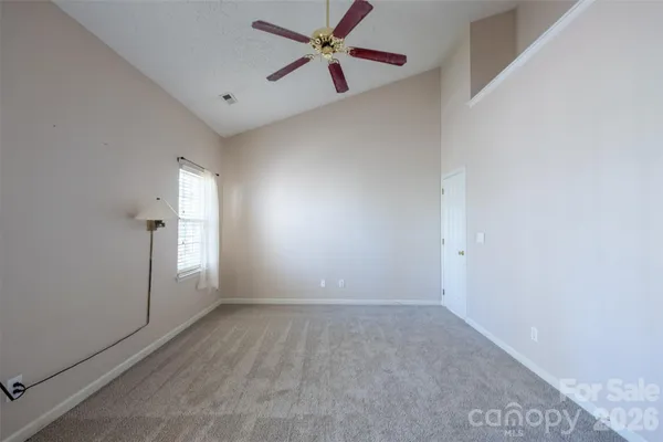 an empty room with chandelier fan and windows