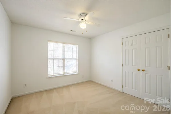 an empty room with chandelier fan and windows