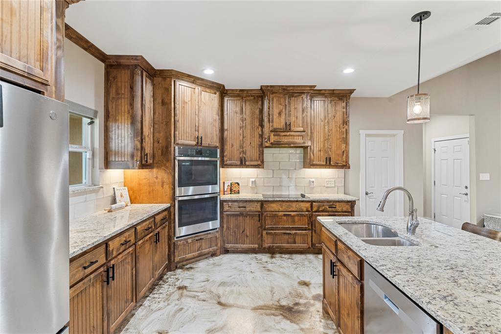 139 Kriston Lane Springtown, TX 76082 - Photo 10 of 39 Kitchen featuring wood cabinetry, light-toned countertops, a stainless steel double oven, and a centered island with an undermount sink