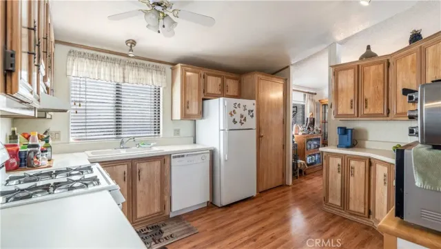 a kitchen with stainless steel appliances granite countertop a refrigerator a sink dishwasher a stove and white countertops with wooden floor