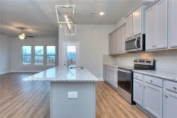 a kitchen with stainless steel appliances granite countertop a sink dishwasher a microwave oven a stove with white cabinets and wooden floor