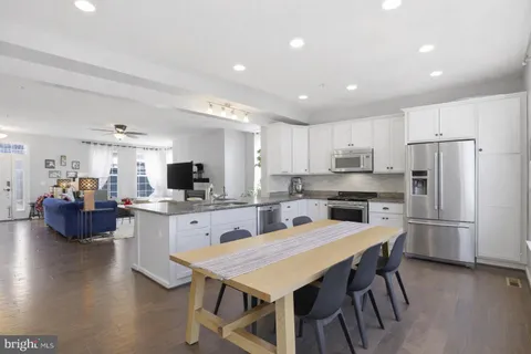 a kitchen with stainless steel appliances kitchen island granite countertop a dining table chairs refrigerator and microwave