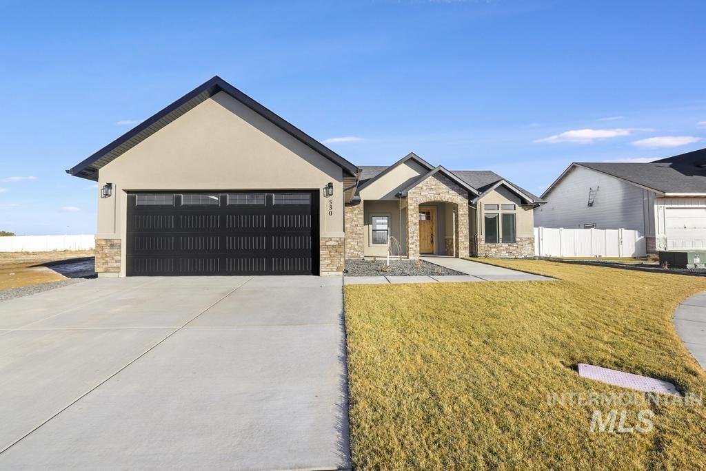 View of front of property featuring stone siding, stucco siding, concrete driveway, a front lawn, and a garage