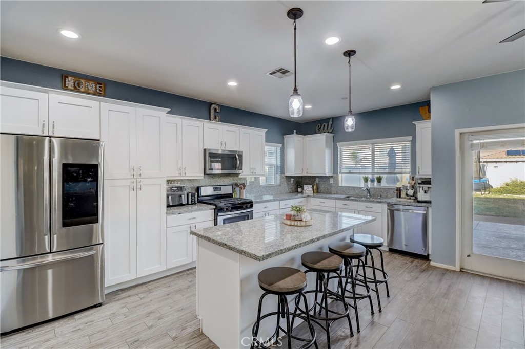 1667 Constant Trail San Jacinto, CA 92582 - Photo 11 of 44 a kitchen with stainless steel appliances granite countertop a refrigerator a stove a sink a center island a dining table and chairs with wooden floor