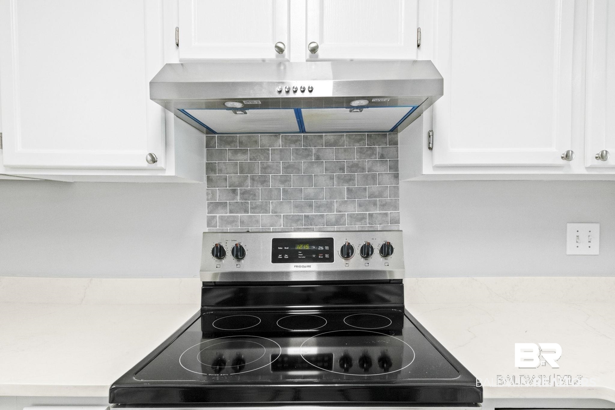 25861 Canal Road, Unit 77 Orange Beach, AL 36561 - Photo 21 of 48 Kitchen view of range hood, stainless steel electric range, backsplash, white cabinetry, and light stone counters