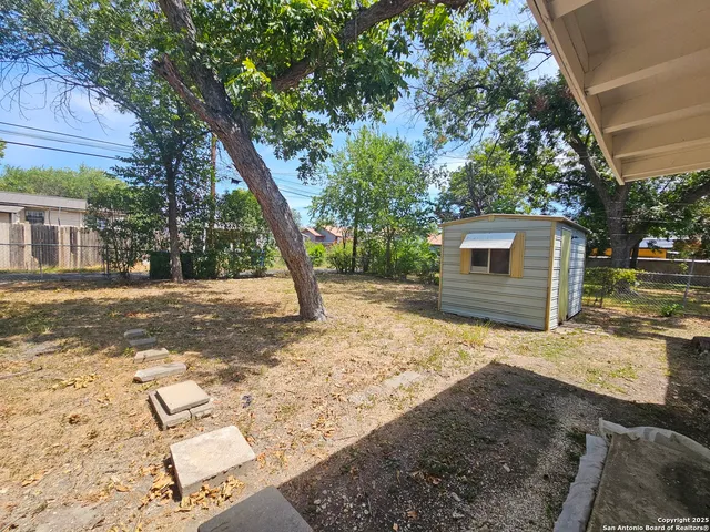 a backyard of a house with large trees and wooden fence