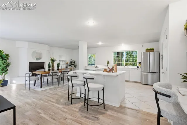 a kitchen with stainless steel appliances kitchen island granite countertop a refrigerator a stove a dining table and chairs with wooden floor
